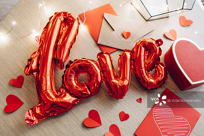情人节概念，红色爱心气球、纸质心形、心形礼品盒和信封放在木桌上图片素材