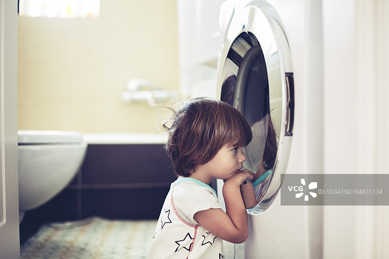 孩子好奇地看着洗衣机里的衣物旋转图片素材