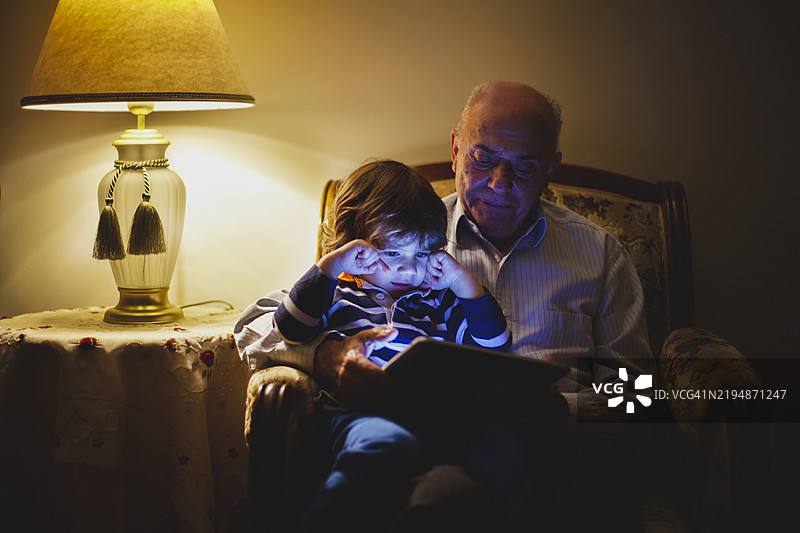 祖父和孙子在温馨的房间里通过平板电脑建立联系图片素材