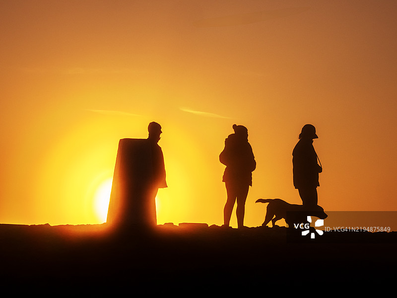 在英国兰开夏郡里布尔谷的彭德尔山三角点旁，一家人和他们的狗在日出时分。图片素材