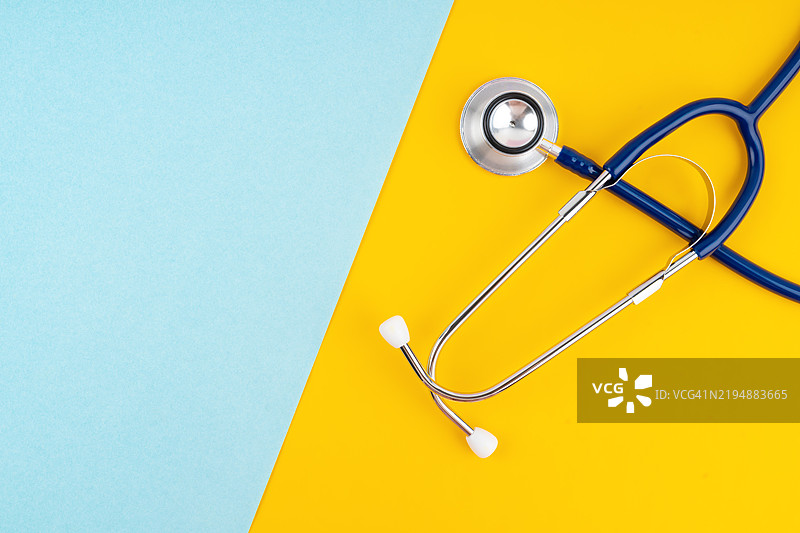 听诊器置于明亮的黄色和蓝色背景上，留有空白区域。图片素材