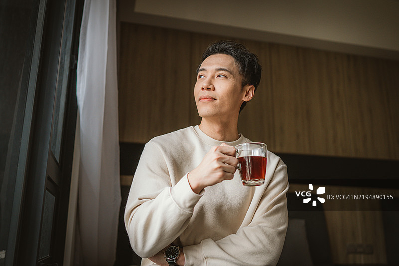 年轻的亚洲男子在家中站着喝咖啡图片素材
