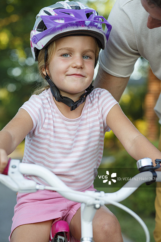 小女孩在父亲的帮助下学习骑自行车图片素材