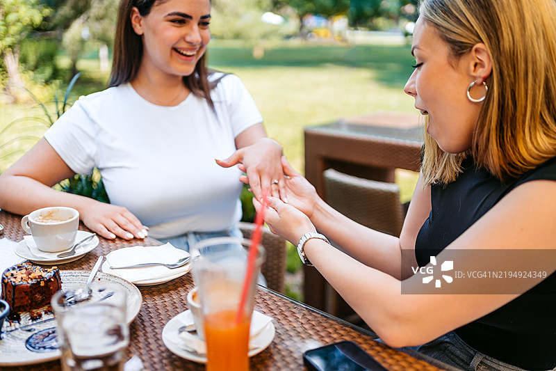 年轻女性在户外咖啡馆向她的女性朋友展示她的订婚戒指图片素材