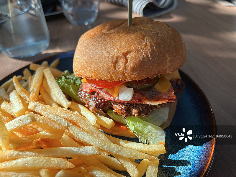 户外咖啡馆桌子上的培根芝士汉堡和薯条图片素材