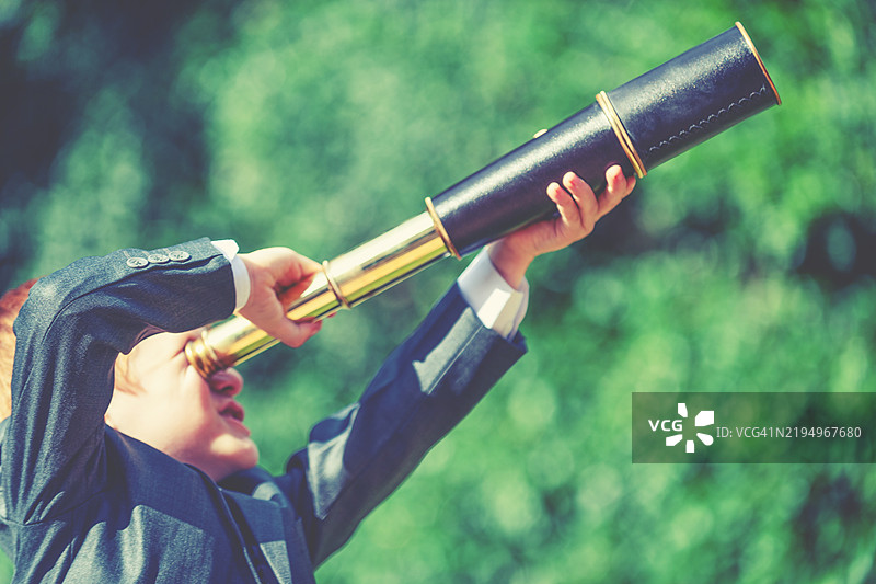 一个穿着商务西装的孩子在用望远镜观察图片素材