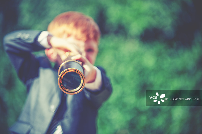 一个穿着西装的孩子通过望远镜寻找商业机会。图片素材