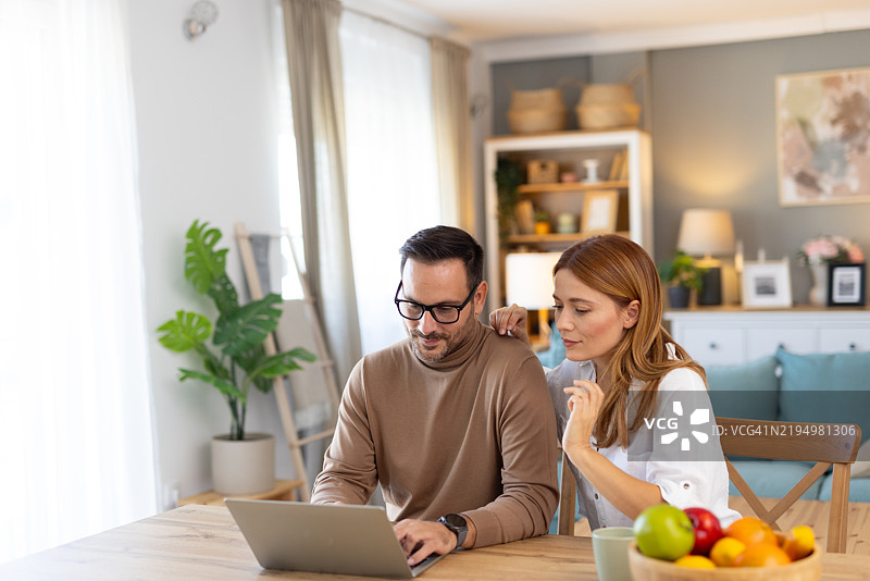 在明亮的客厅中，情侣一起合作使用笔记本电脑图片素材