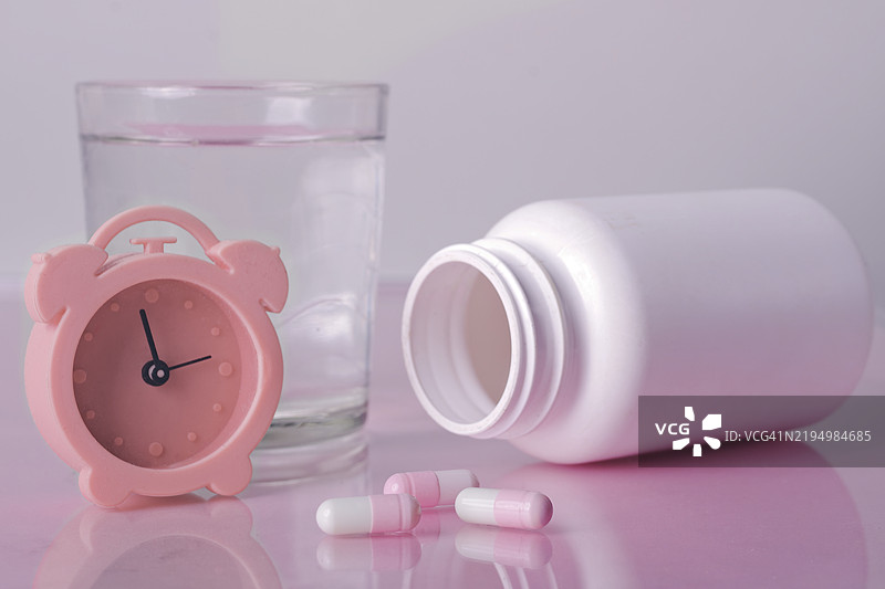 粉色闹钟旁边放着一杯水和药物，失眠概念，德国图片素材