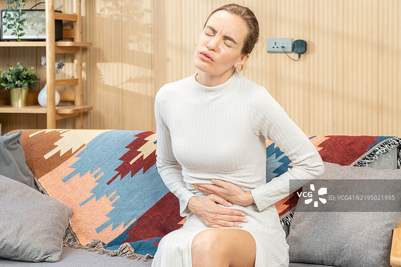 年轻女性在家中因胃痛而痛苦，特写。食物中毒图片素材