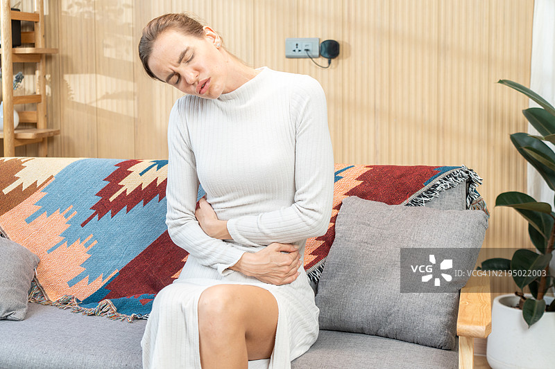 年轻女性在家中因胃痛而痛苦，特写。食物中毒图片素材