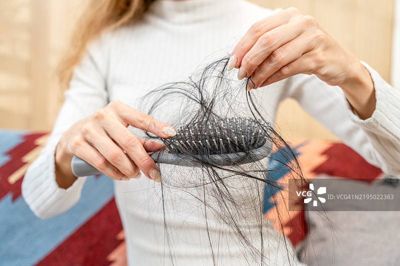 女性的手拿着一把掉落许多头发的发刷，可能是由于脱发、贫血或产后疾病。图片素材