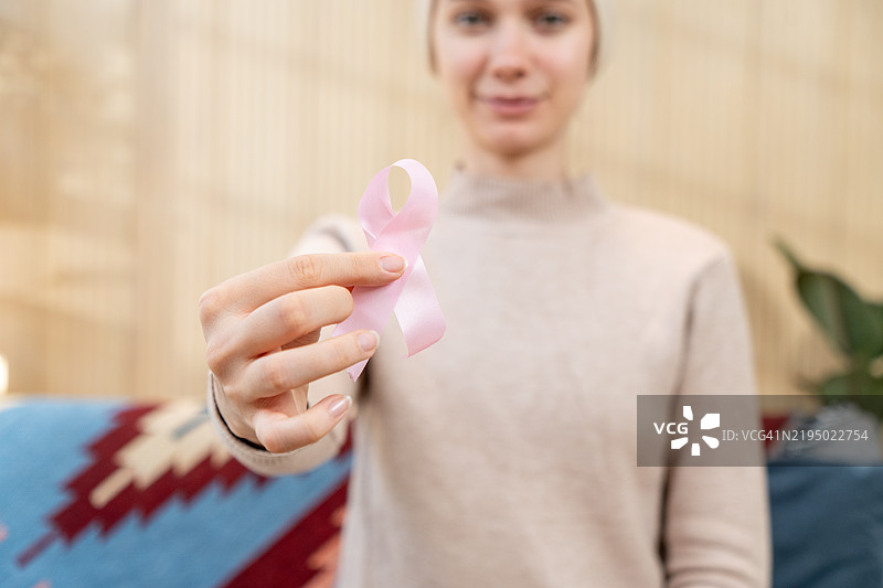 一位光头女性手持粉色癌症意识丝带，象征着对这一事业的支持。图片素材