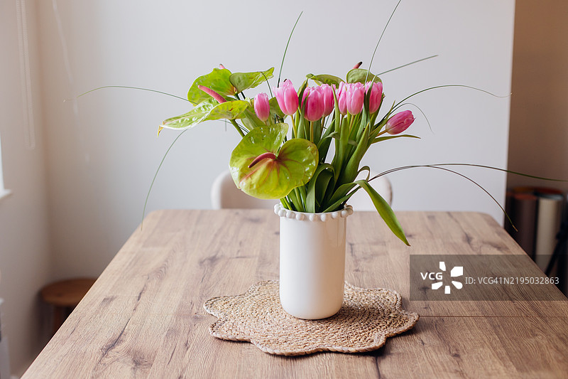 白色陶瓷花瓶中的春季花束。粉色郁金香和绿色亮丽的马蹄莲。春天、复活节和母亲节的节日概念。图片素材