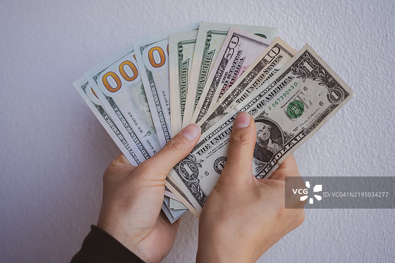 手持各种美金钞票的特写镜头，背景为白色墙壁。图片素材