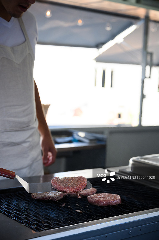 男性街头小吃摊贩在烤架上翻转汉堡肉饼图片素材