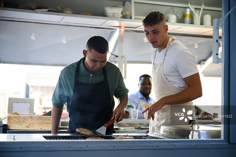 厨师在城市餐车上指导副厨师如何烹饪汉堡。图片素材