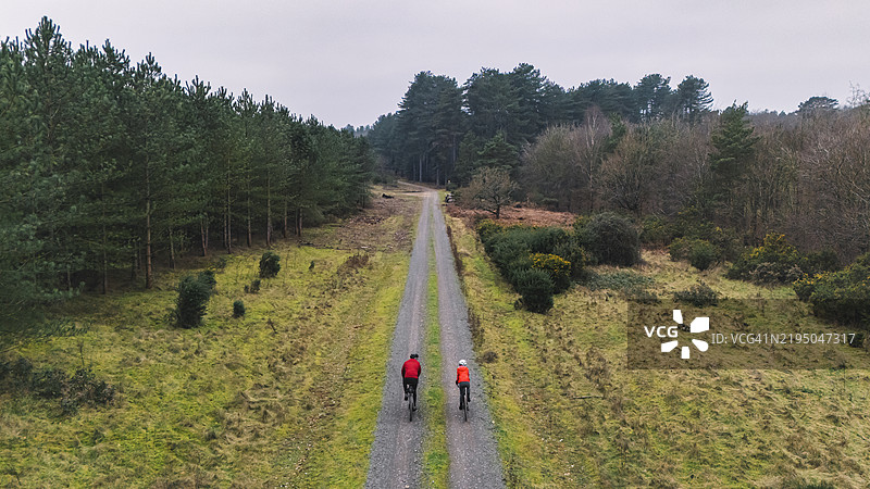 一位成熟男性与他的青少年女儿在森林中骑自行车的高角度后视图图片素材