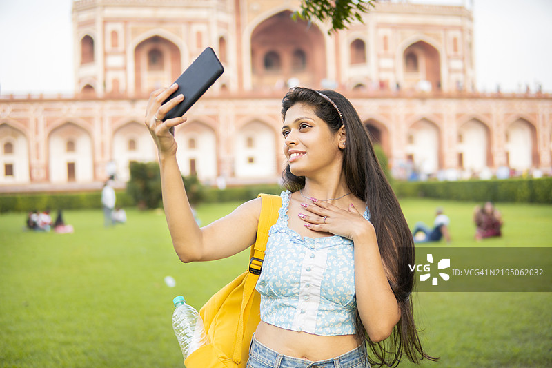 快乐的年轻女性游客在胡马雍陵前用手机自拍。图片素材