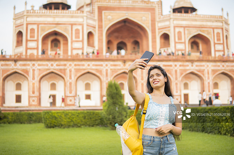 快乐的年轻女性游客在胡马雍陵前用手机自拍。图片素材