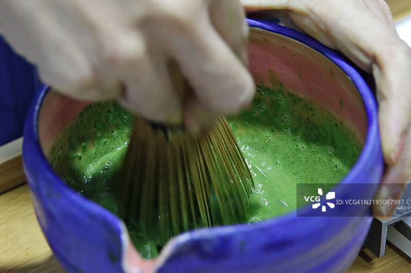 特写镜头：女性手持日本茶杯和茶筅，在桌上制作、搅拌和准备浓茶抹茶热饮。图片素材