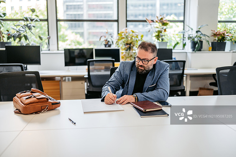 中年男子在澳大利亚悉尼的办公大楼内的桌子上写笔记本。图片素材