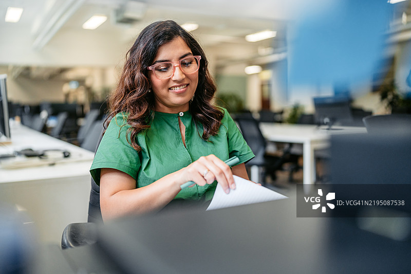 中年印度女性在澳大利亚悉尼的办公大楼内的桌子上写笔记。图片素材