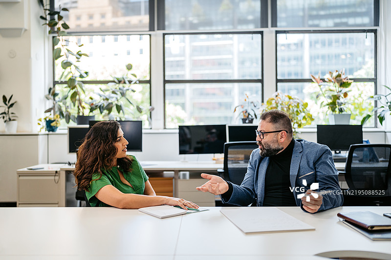 两位中年同事在澳大利亚悉尼的办公室桌前交谈图片素材