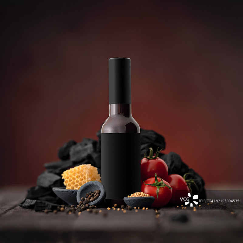 瓶装的番茄酱，加入蜂蜜和芥末，黑色炭火放在木桌上。烟熏甜酱的配料。烧烤酱，番茄酱，酸辣酱。调味品。食品概念。红色背景。留白空间。图片素材