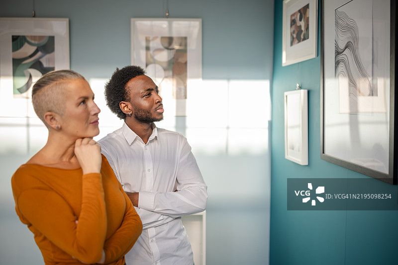 参观者在明亮的蓝色墙壁画廊中欣赏当代艺术展览的抽象艺术作品图片素材