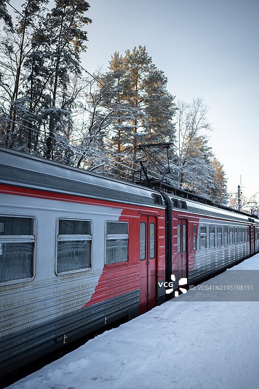电动火车在雪覆盖的森林中穿行，清晨的阳光洒在蓝天上。图片素材