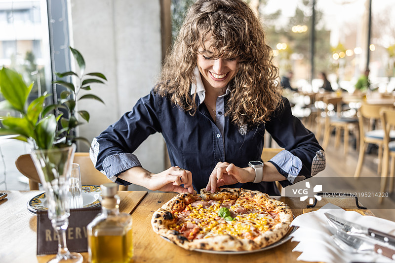 可爱的卷发年轻女性在餐厅里用双手捧着刚出炉的比萨饼图片素材