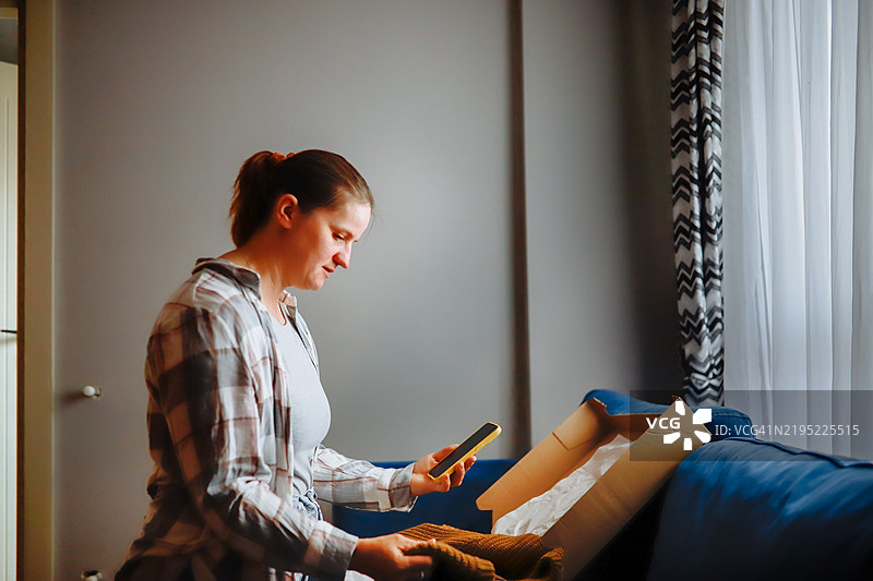 中年女性在家沙发上打开盒子里的毛衣。图片素材