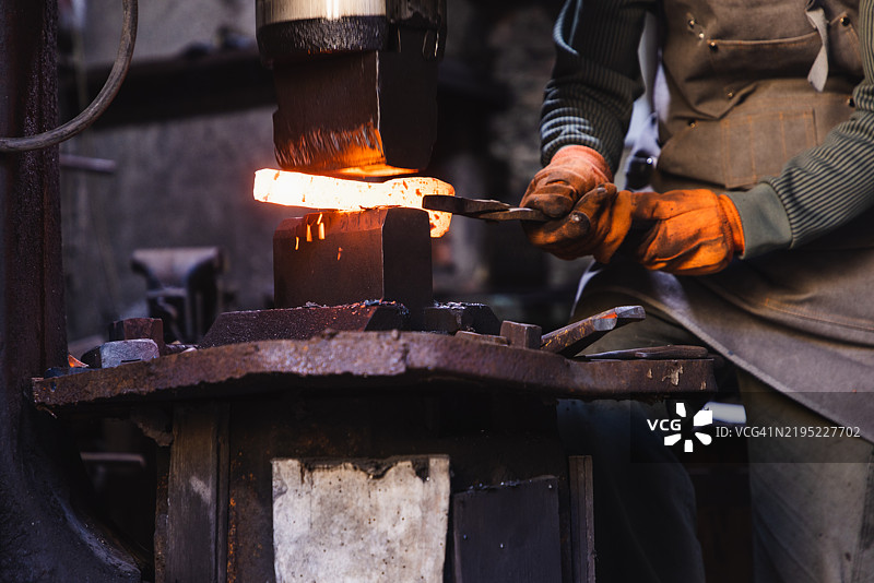 亚洲铁匠使用动力锤锻造金属棒图片素材