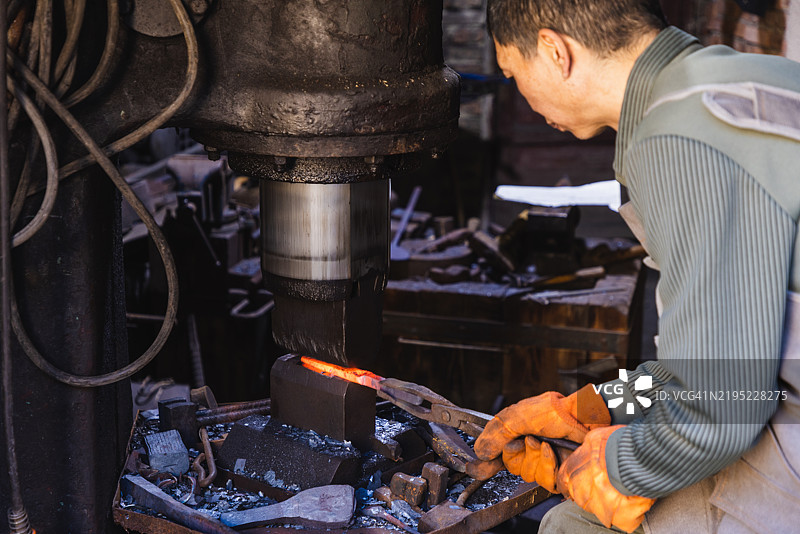 亚洲铁匠使用动力锤锻造金属棒图片素材