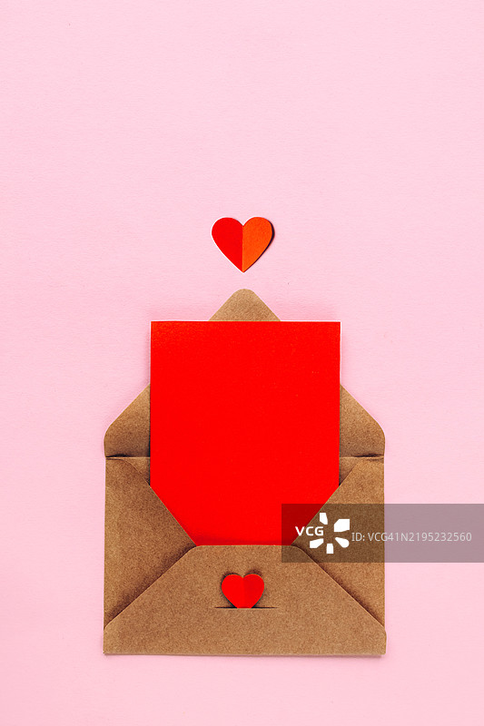 打开的牛皮纸信封，里面有红色卡片和纸质心形装饰，背景为粉色。情人节，母亲节贺卡。图片素材