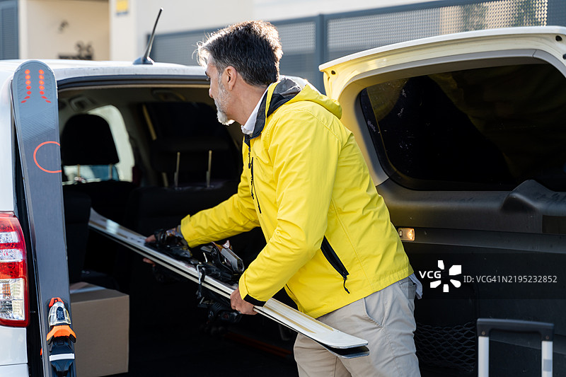 成熟男子在滑雪旅行前将滑雪板装入汽车后备箱图片素材