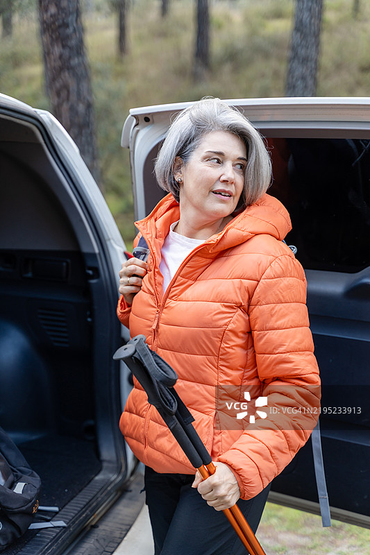 一位年长女性从汽车后备厢取出登山杖，准备去徒步旅行。图片素材
