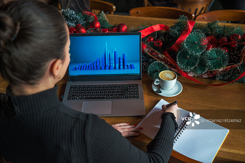 在咖啡馆温馨的氛围中，一位女商人正专注地在笔记本电脑上分析财务图表，手中端着一杯咖啡。从鸟瞰角度拍摄的场景展现了精致的企业风格和充满活力的商业生活方式。图片素材