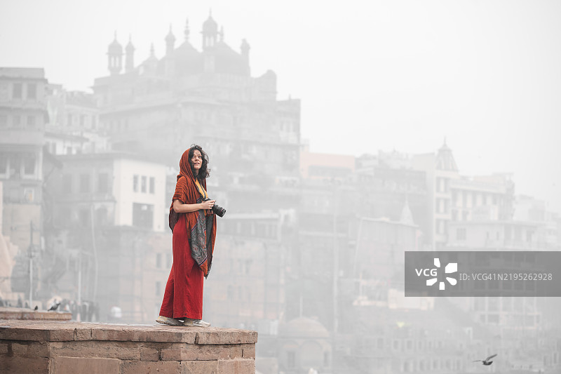 身穿鲜艳红色服装的女性在历史悠久的瓦拉纳西探索并拍照图片素材