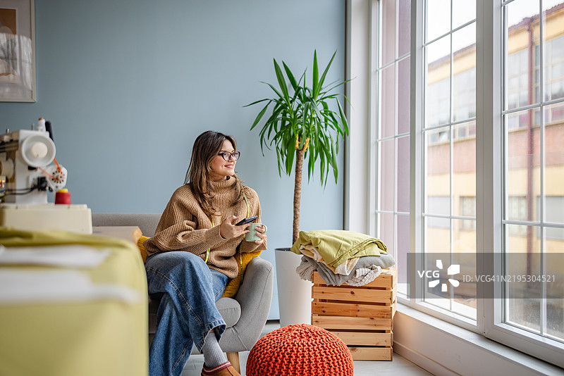 女人在阳光明媚的下午，坐在大窗户旁享受舒适的时光，喝着茶，放松身心。图片素材
