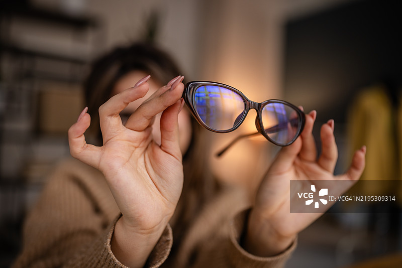 女性在舒适的室内环境中展示时尚的猫眼眼镜，正值白天。图片素材