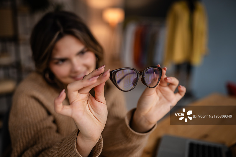 女性在舒适的室内环境中坐在木桌旁展示时尚眼镜图片素材