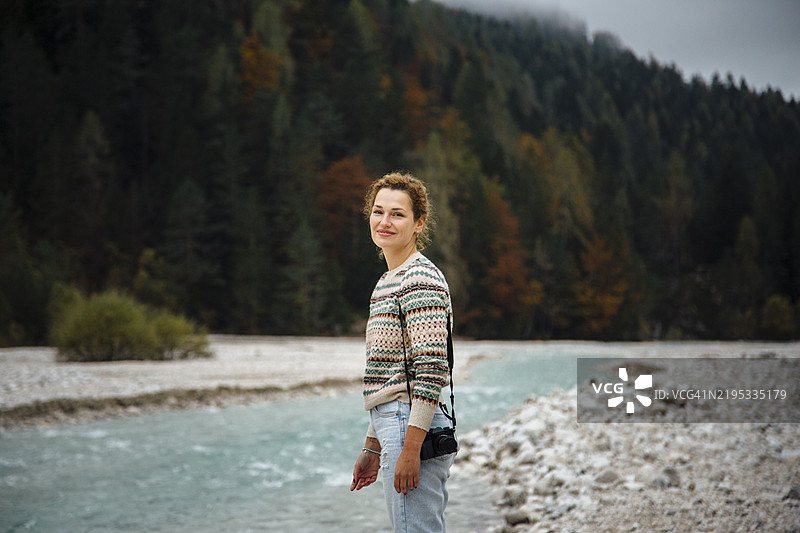 一位手持相机的游客，背景是山脉和山间河流。图片素材