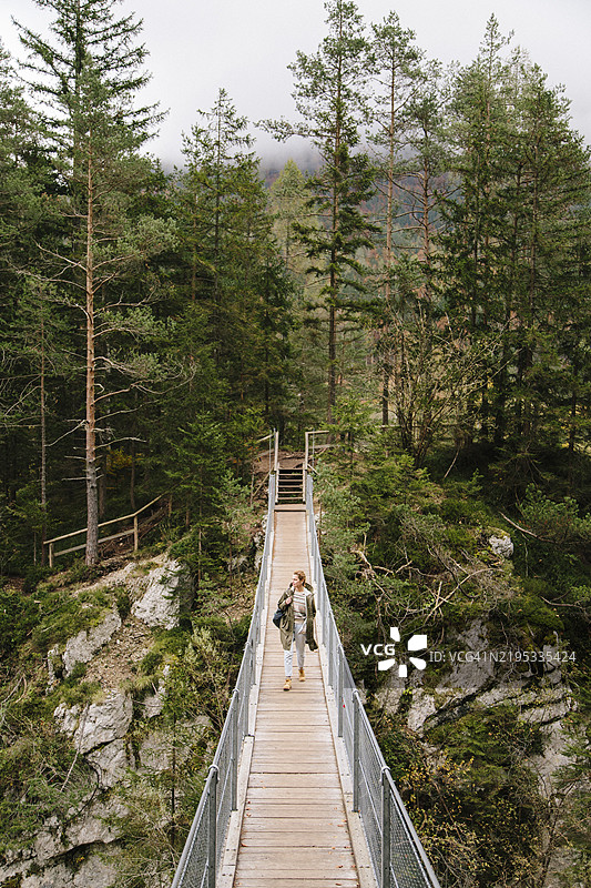 女性在户外徒步旅行，走在悬索桥上的竖拍照片图片素材