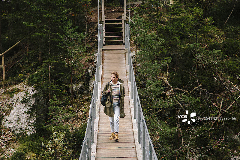 女徒步旅行者走在悬索桥上，下面是山间河流。图片素材
