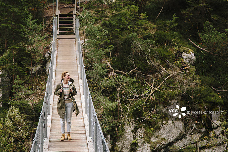 穿着雨衣、背着背包的女性在吊桥上徒步旅行图片素材