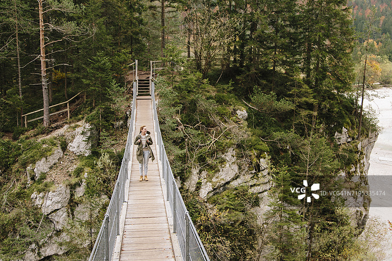 年轻女性旅行者走在山间河流上的桥上图片素材