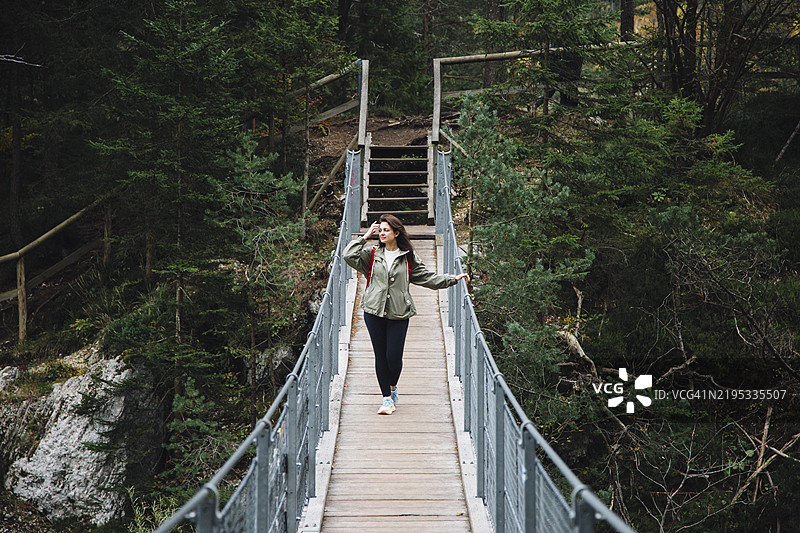 穿着休闲服的女性在树林中的悬索桥上行走图片素材