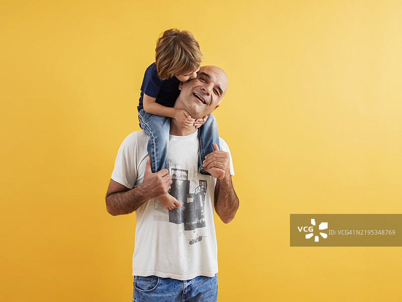 父亲和儿子在黄色背景下分享快乐时光图片素材